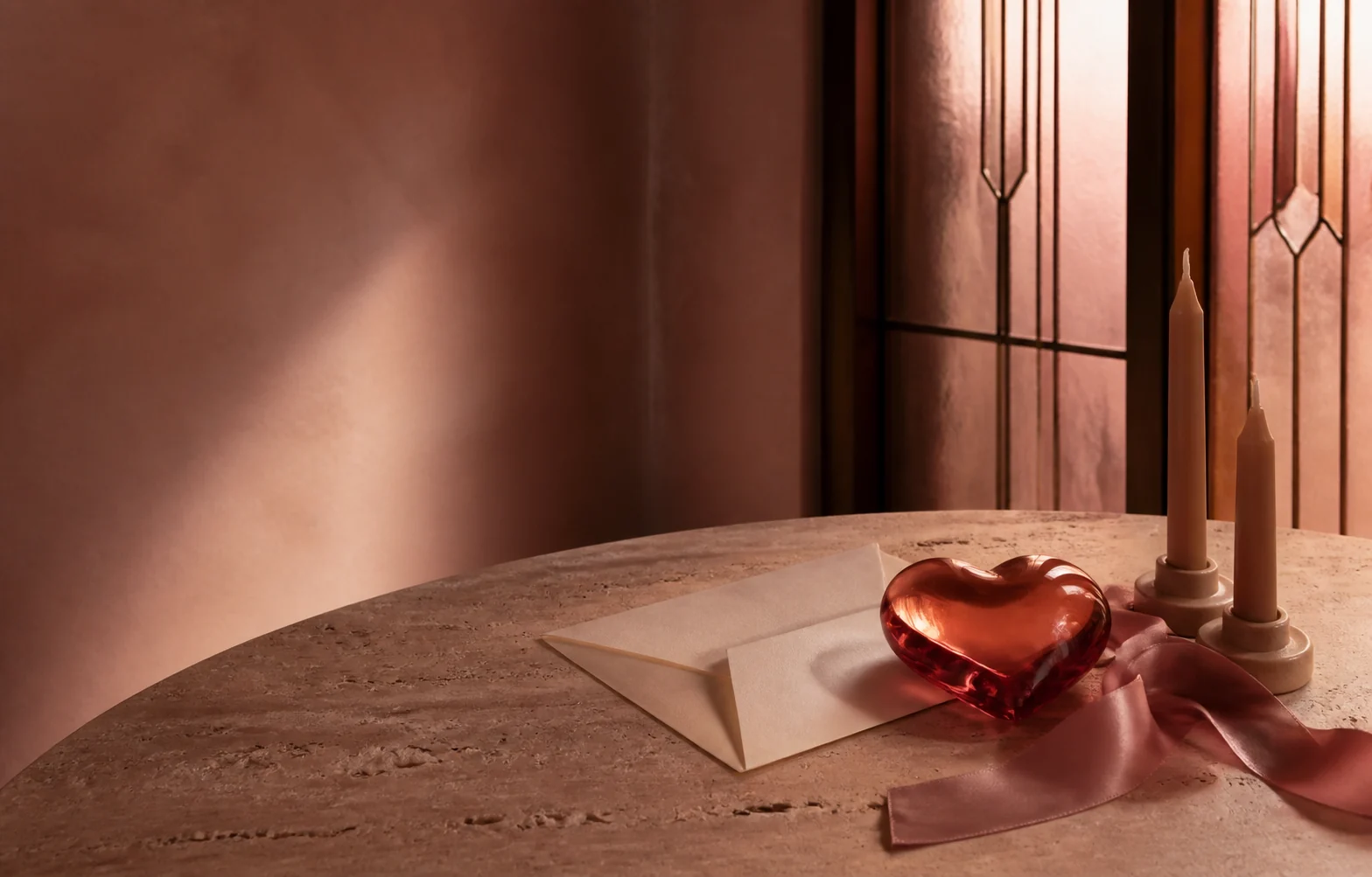 Coral glass heart, folded letter, silk ribbon and unlit candles on a stone table